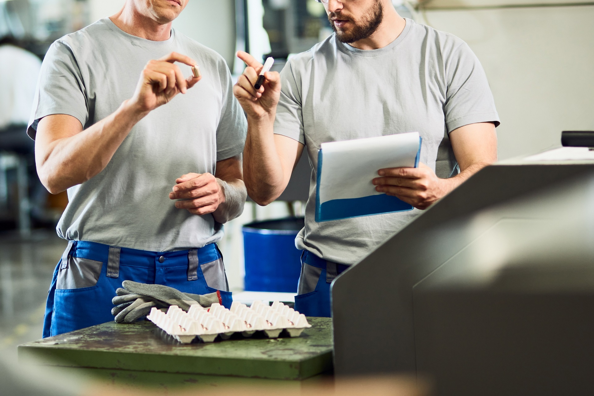 Dwóch pracowników omawia oprzyrządowanie do maszyn CNC w zakładzie produkcyjnym. Narzędzia CNC w tle.